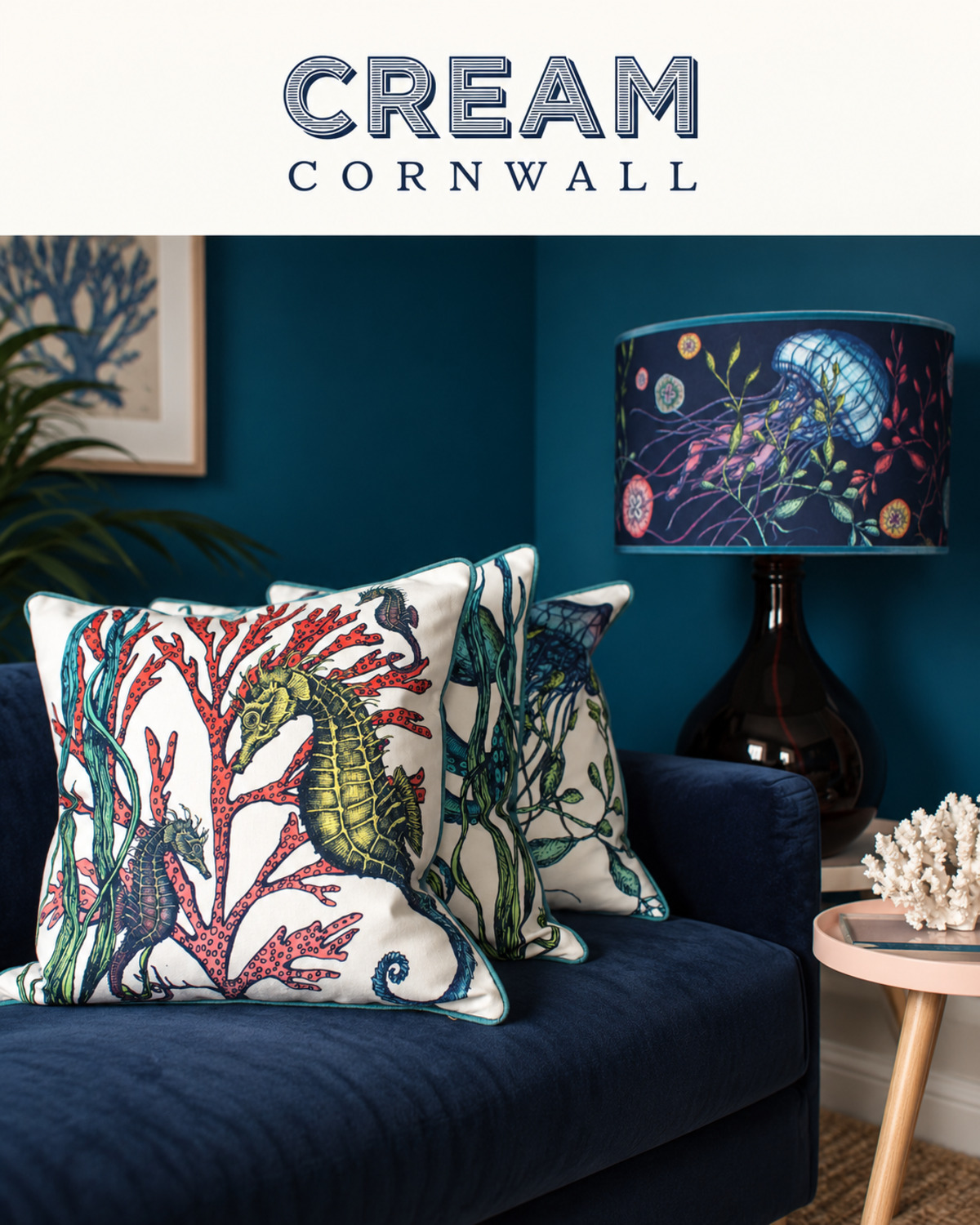 Cream Cornwall cushions printed with seahorses, coral and seaweed on a navy velvet sofa, beside a jellyfish-print lampshade, under the Cream Cornwall logo. Illustrative layout, not an original campaign screenshot.