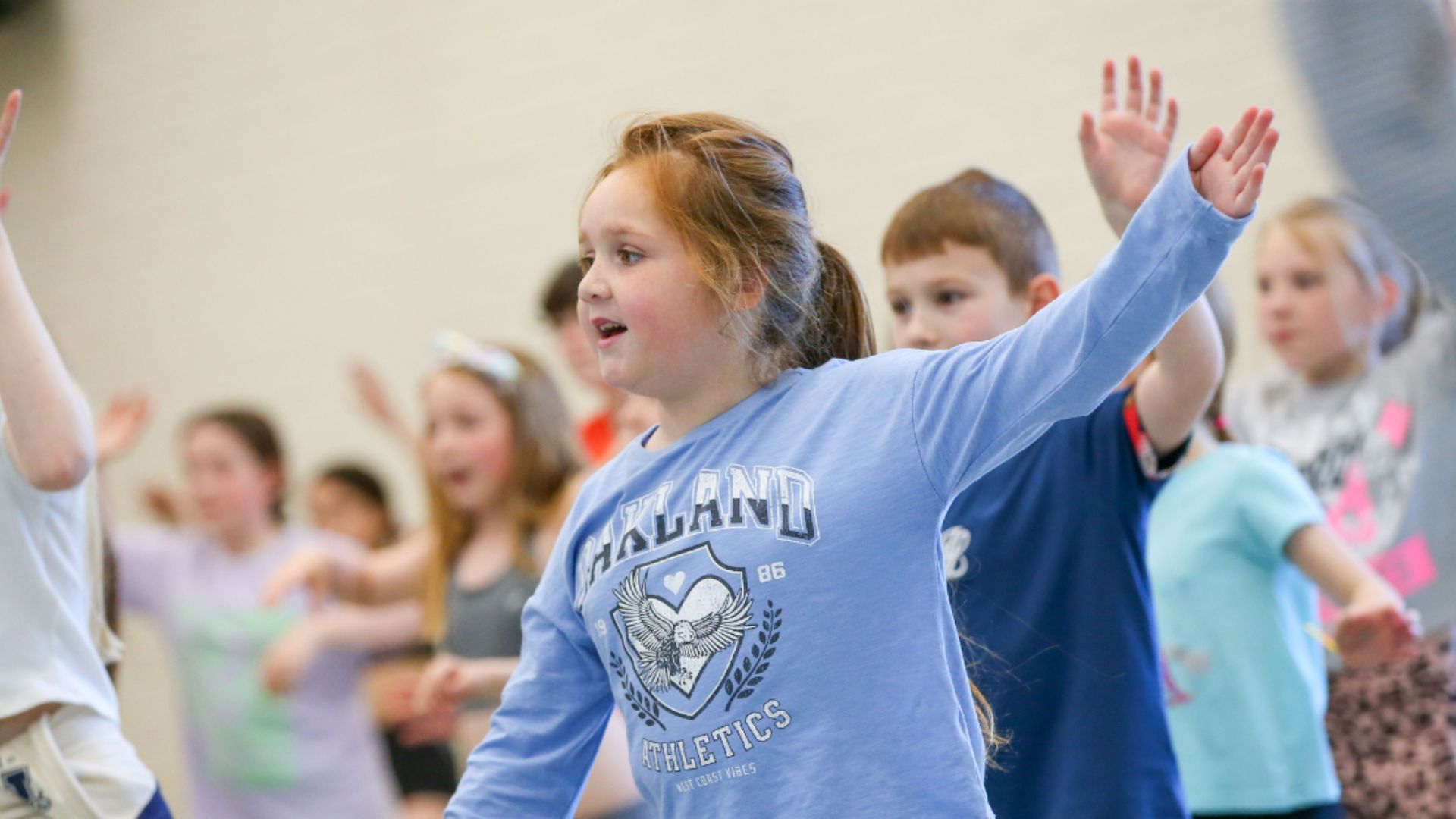 Children in a Dance City community class, arms raised mid-movement in a bright studio