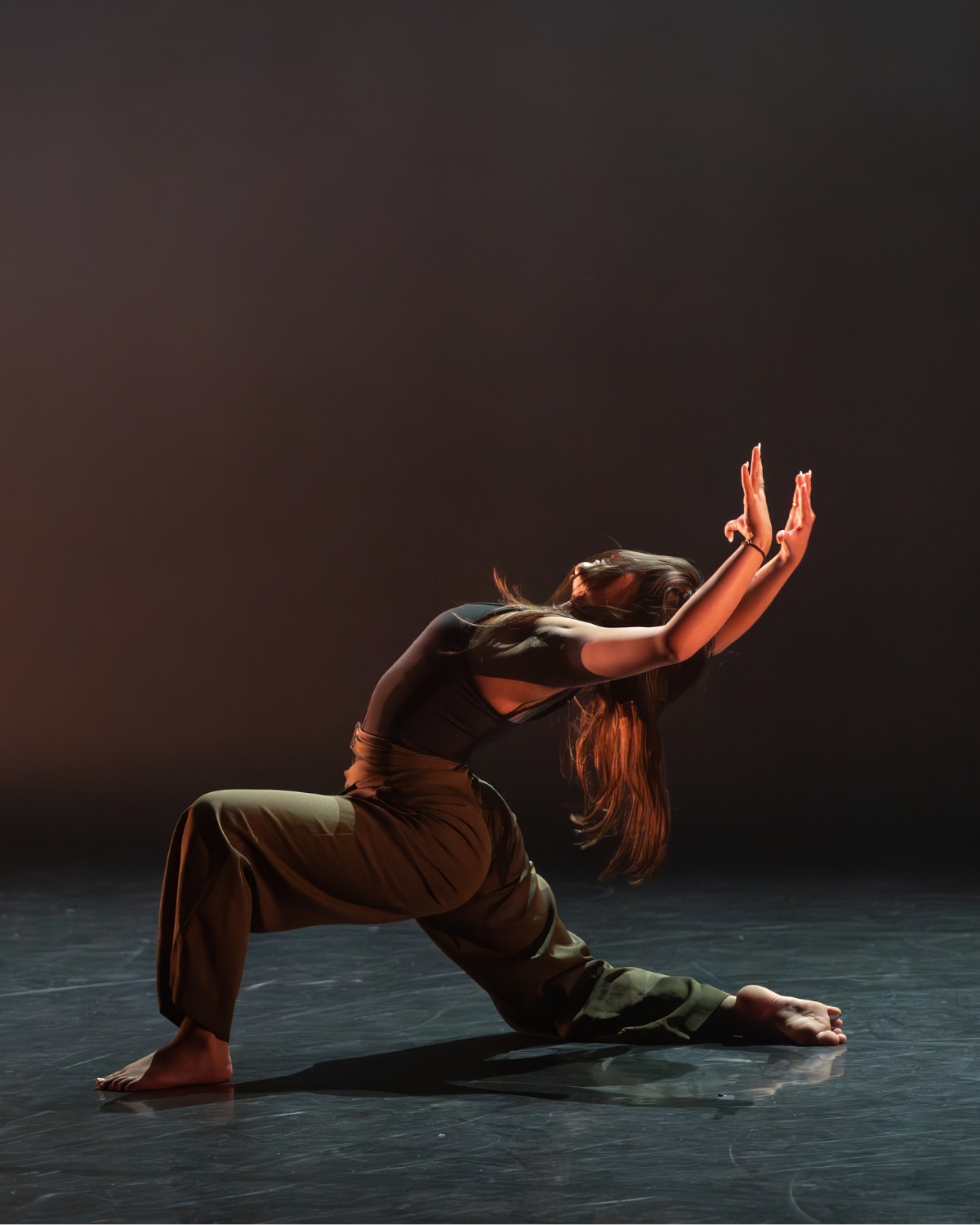 A solo contemporary dancer in a deep lunge under warm stage light, arms raised
