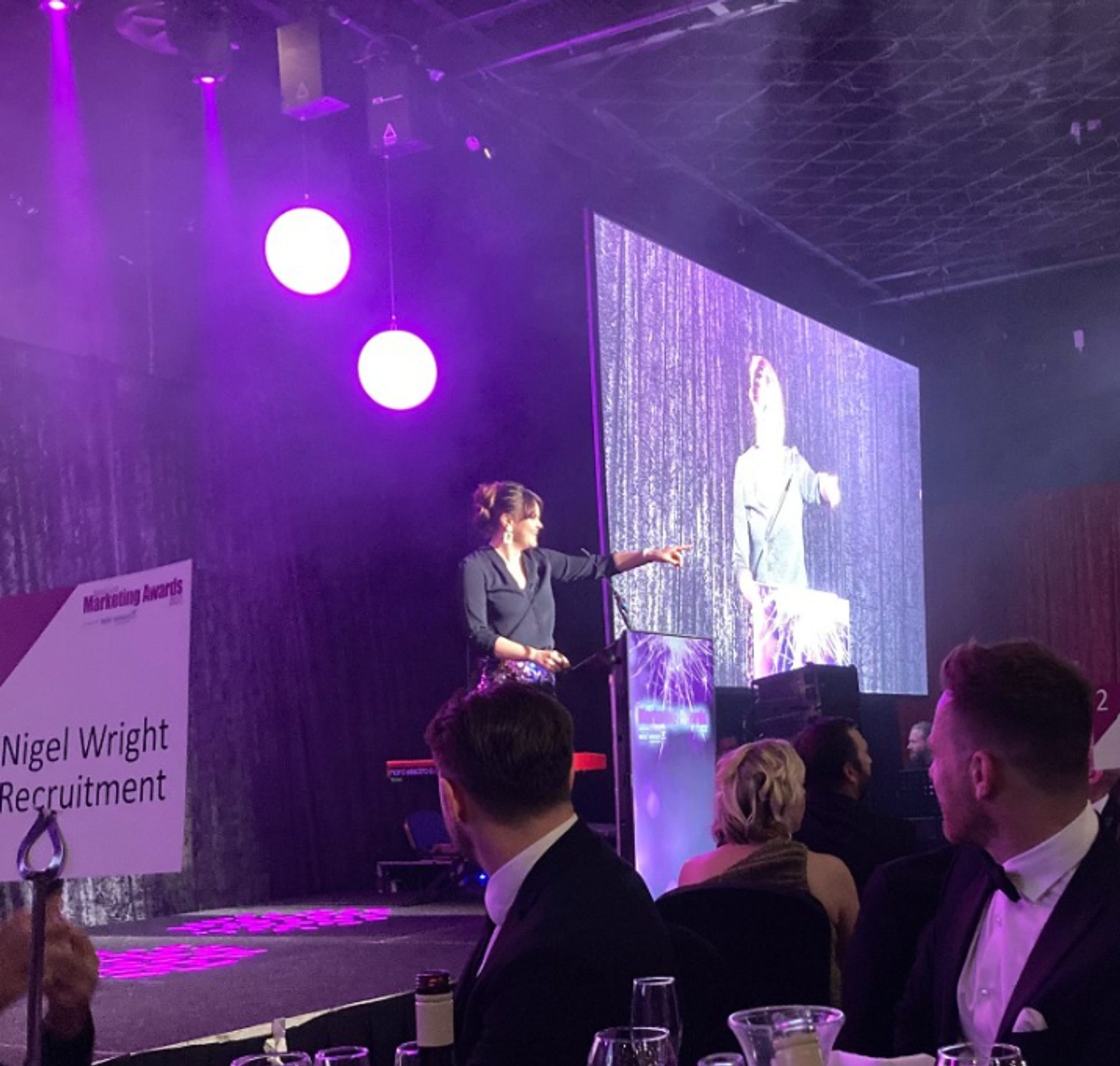 The host on stage at the North East Marketing Awards ceremony, beside a Nigel Wright Recruitment sign